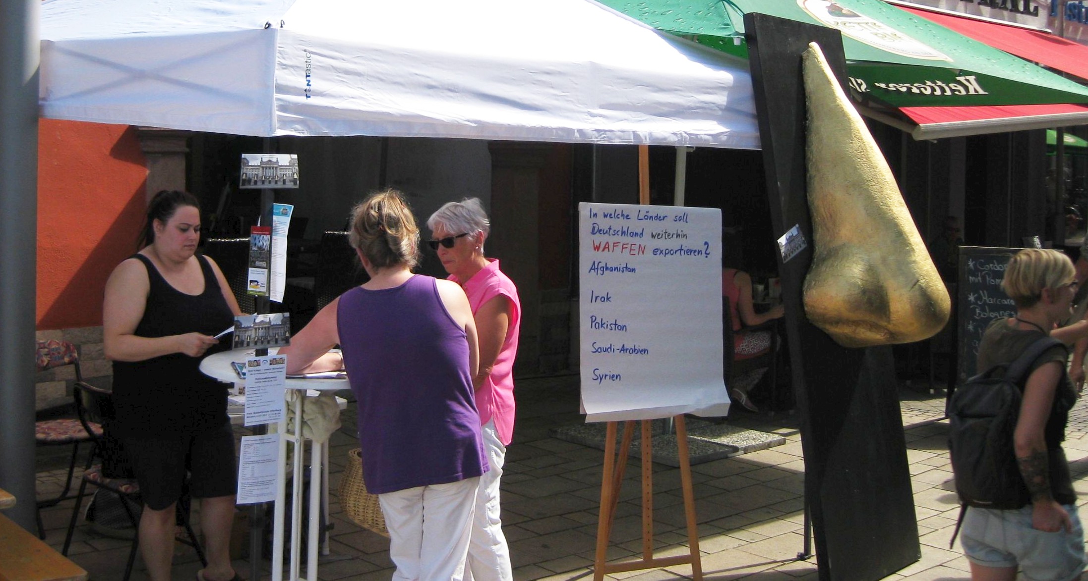 Foto eines Standes mit Pavillon und 4 Personen, sowie einer übergroßen vergoldeten Nase und einem Fragebogen
